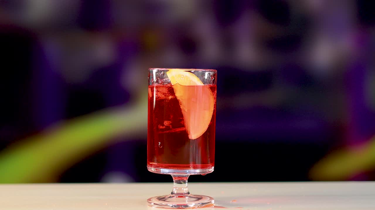 Un cocktail Negroni viene preparato con una guarnizione d'arancia in un ambiente vivace. L'illuminazione brillante esalta il colore intenso della bevanda.