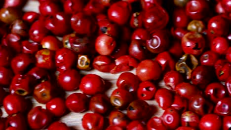 granos de pimienta pimienta rosa colorida en extrema cámara lenta caen en una superficie de madera y se mezclan entre sí