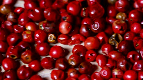 grains of pepper pink pepper colorful in extreme slow-motion fall on a wooden surface and mingle with each other