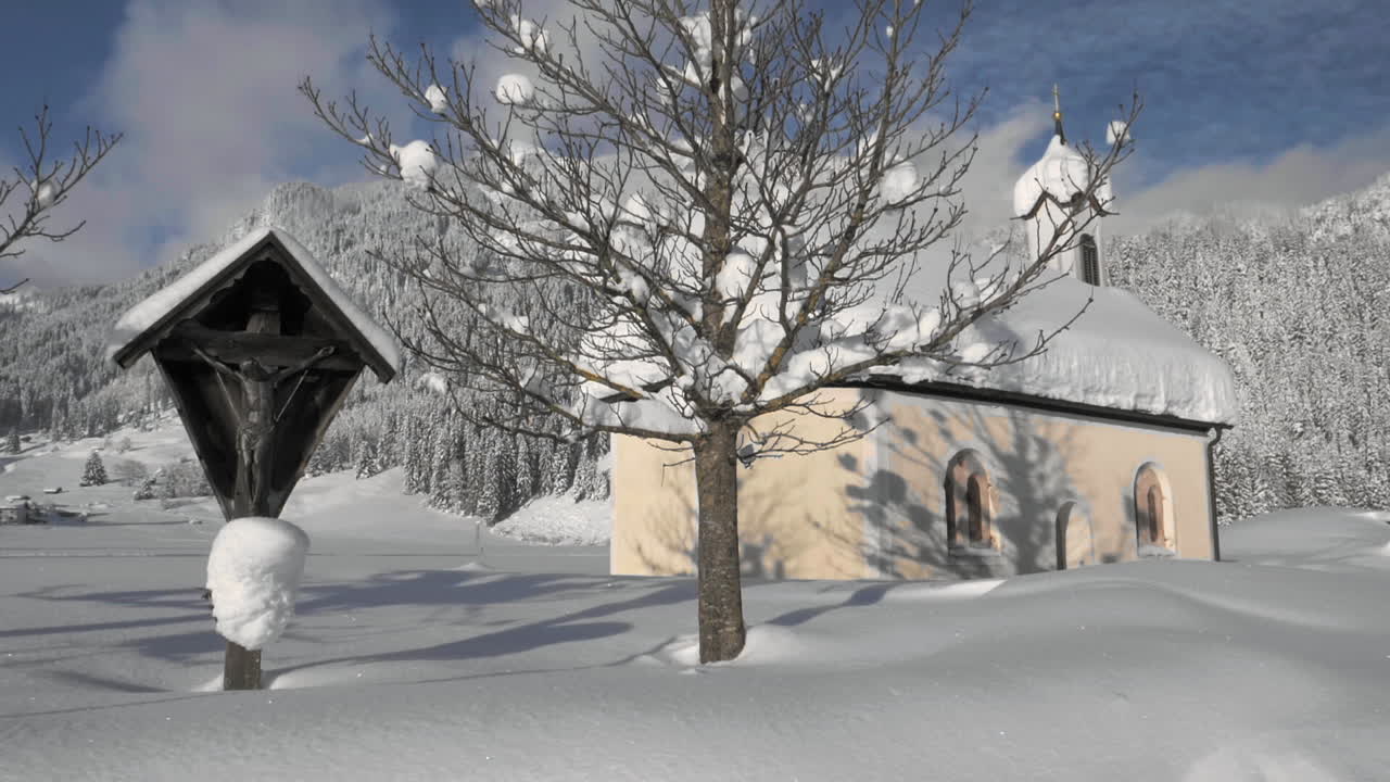 Gimbal shot showing a snowy landscape in in the sunshine of the Tyrol, Austria and revealing a snow covered tiny chapel in Lechaschau