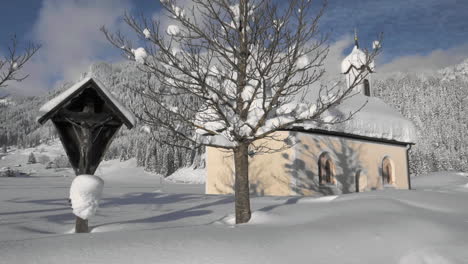 gimbal shot showing a snowy landscape in in the sunshine of the tyrol, austria and revealing a snow covered tiny chapel in lechaschau