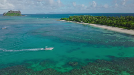 aerial drone follows tour boat speeding across turquoise water over coral reef