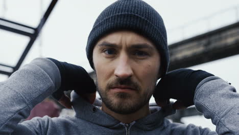 close-up view of caucasian bearded caucasian man in grey hoodie and boxing to the camera outdoors an abandoned factory on a cloudy morning