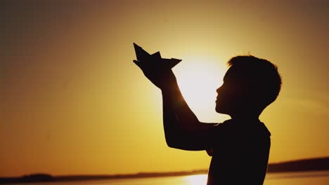 paper boat is in the hands of a child. beautiful summer sunset. origami
