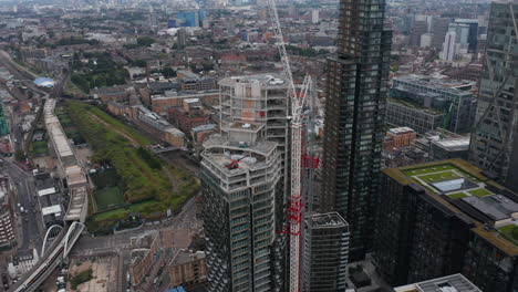 Fly-around-construction-site-of-new-skyscraper-in-Shoreditch-district.-Tilt-up-reveal-cityscape.--London,-UK