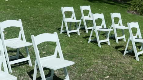 white folding chairs on meadow landscape at outdoor wedding during sunny day