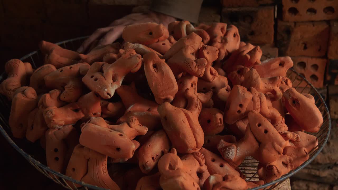 las flautas de arcilla de animales artesanales se apilan en una canasta de metal en thanh ha, vietnam, mientras una mano agrega una, perfecta para el turismo y los recuerdos