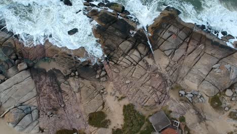 drone moving away from ocean rock shore in punta del diablo, rocha, uruguay