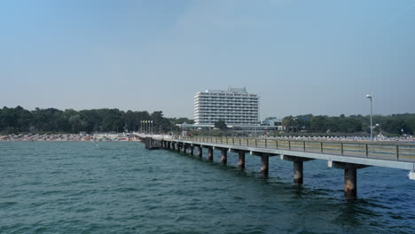 Toma-Amplia-De-Un-Largo-Puente-Peatonal-Con-Playa-De-Arena-Y-El-Famoso-Hotel-Maritim-En-Segundo-Plano-En-Timmendorf,-Alemania