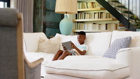 playing with tablet, young boy relaxing on white sofa in living room