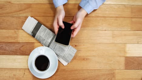 businesswoman using mobile phone at desk with newspaper and cup of coffee on table