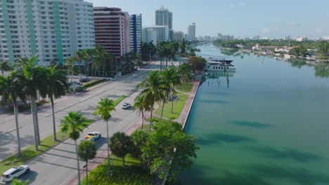 tacking of cars driving on road on waterfront. passing around yachts moored at bank. multistorey apartment buildings in residential borough. miami, usa