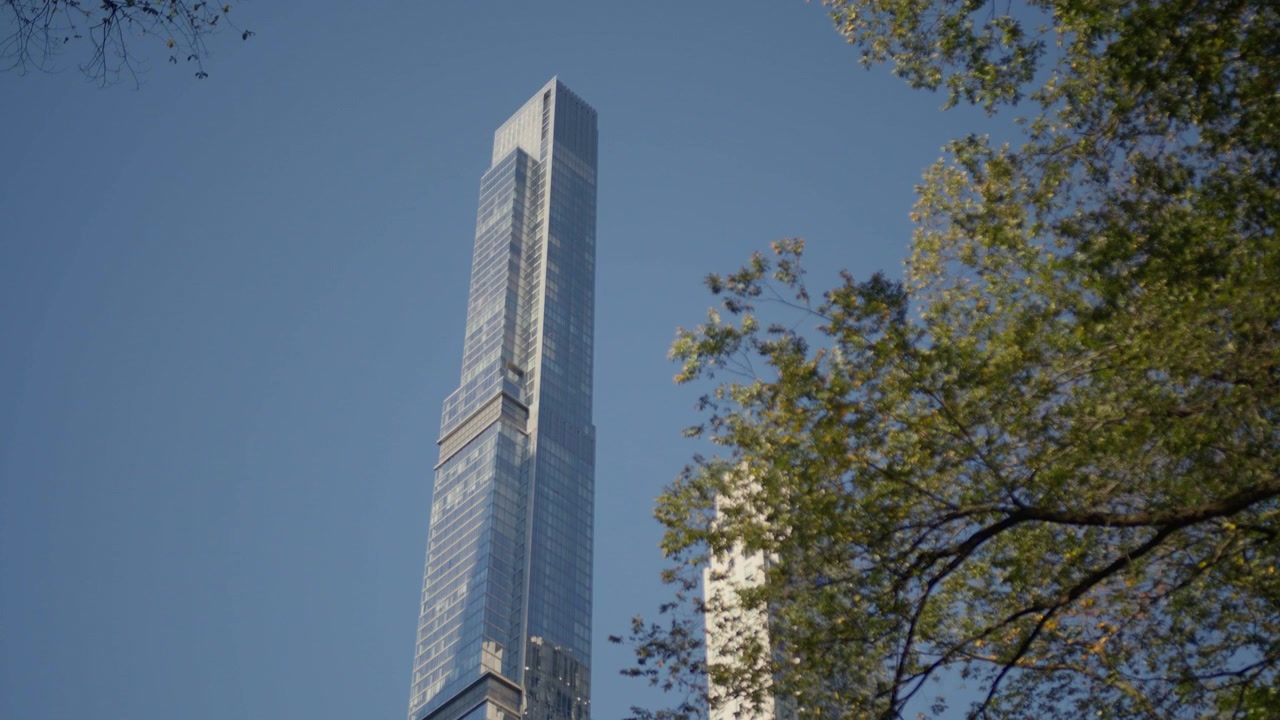 Una torre snella e altissima si innalza in un cielo azzurro e limpido sopra le cime diradate degli alberi autunnali, la sua facciata in vetro cattura il sole basso
