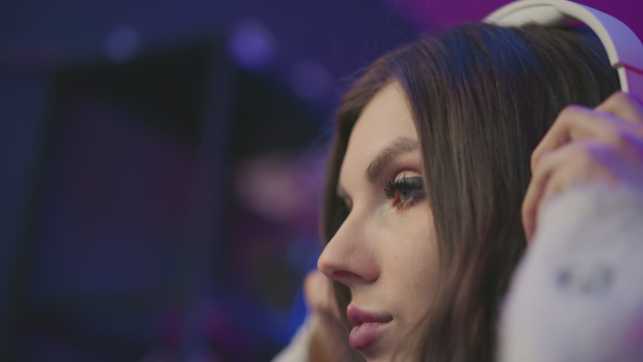 Close up DJ preparing to wear headphones under vivid colorful lighting, focused facial expression, long hair illuminated by ambient lights, suggesting music setup or livestream