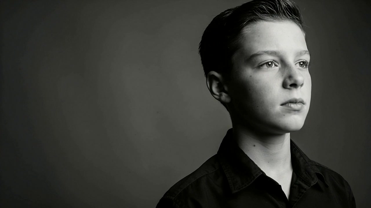 Turning on cue, male teen shifting head, gaze in studio shot wearing black shirt, copy space