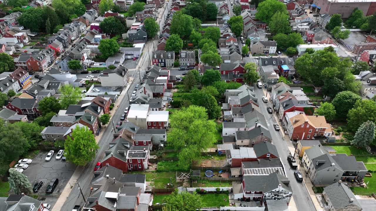 Two straight streets with row of houses in city of United States. Aerial flyover. Green trees in spring. Historic colored townhouses in Lancaster, Pennsylvania.