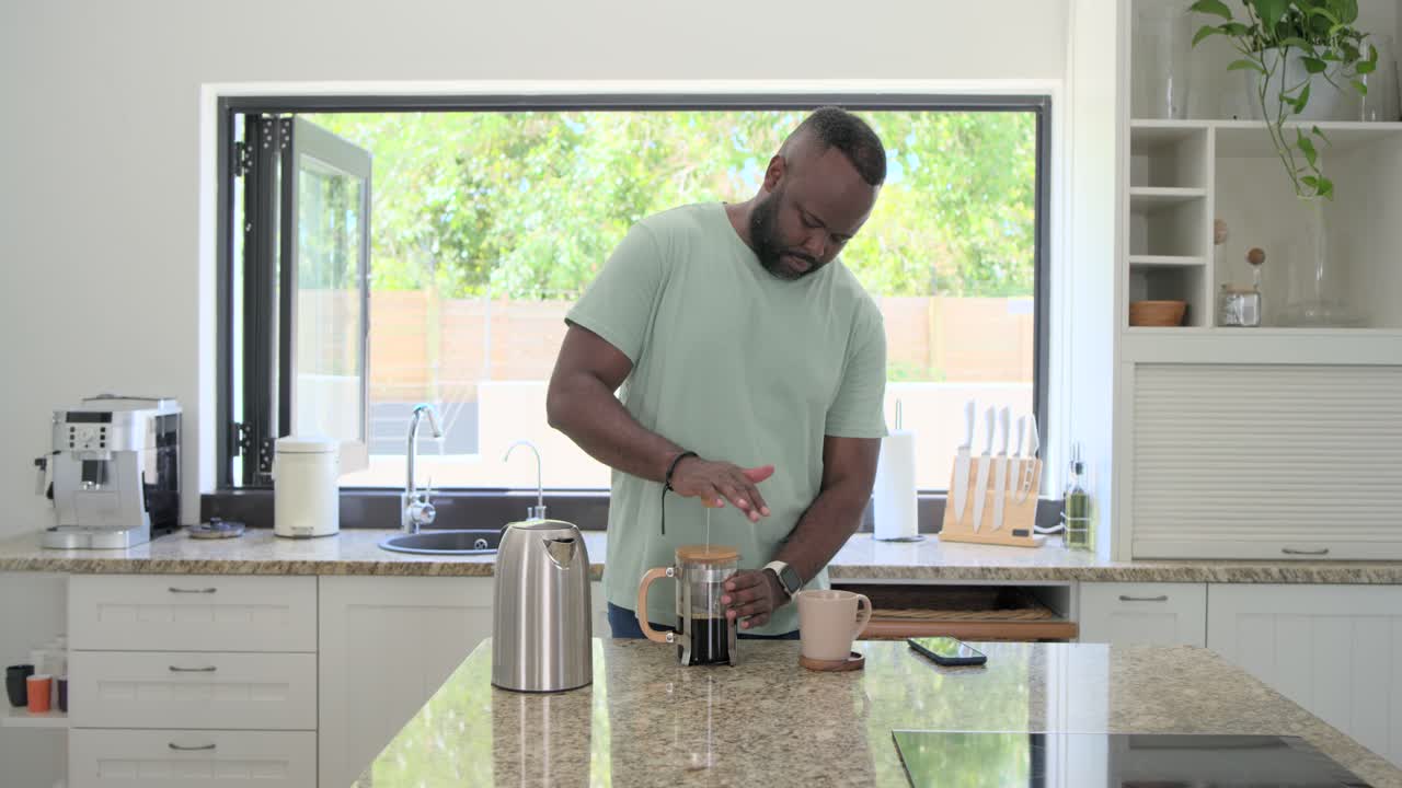 Uomo afroamericano che solleva il bollitore, versa nella French press, e preme lo stantuffo per preparare il caffè.