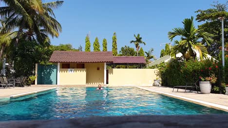 Bearded-middle-aged-white-man-swimming-breast-stroke-towards-camera,-exercising-and-relaxing-in-beautiful,-exotic-outdoor-swimming-pool