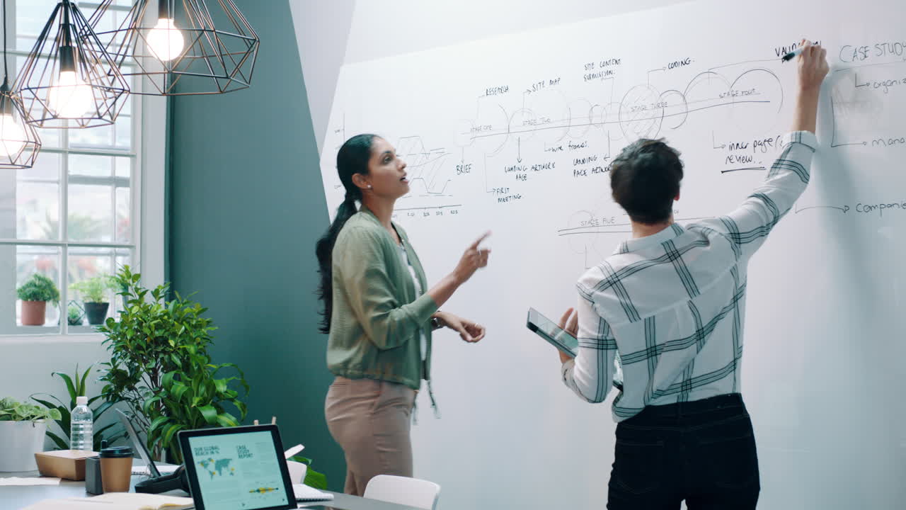Two Women Collaborating and Writing on a Whiteboard in a Modern Office