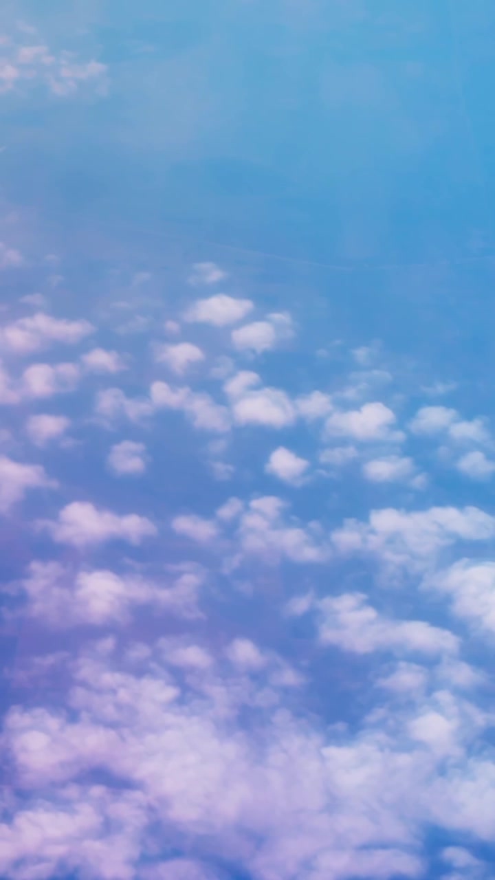 Vertical aerial view of soft scattered clouds below a pale blue sky, creating a dreamy high-altitude atmosphere with calm light and minimal natural beauty.