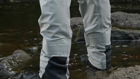 Low-angle-shot-of-a-fisherman-standing-in-full-waders-with-water-flowing-past