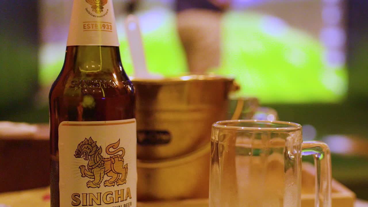 Un primo piano di una bottiglia di birra e un bicchiere con uno sfondo di simulatore di golf.