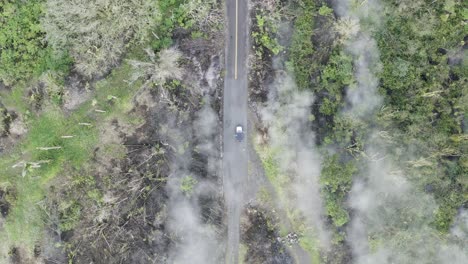 conducción de automóviles en una carretera aislada y estrecha en la isla tropical de hawaii con humo de lava del volcán