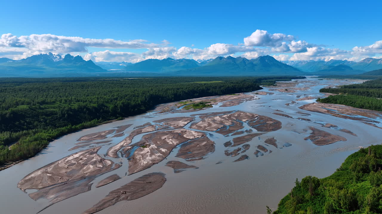 Approaching the shallow branching river in the huge valley surrounded by gorgeous mountains. Stunning panorama of Alaska nature from drone footage