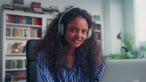 young indian woman sits at table with laptop listening to music on headphones