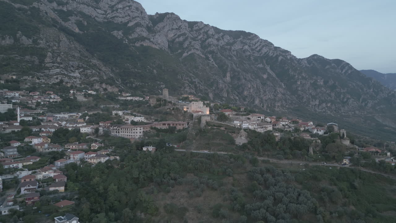 droneshot desde arriba kruje albania volando sobre el castillo en el acantilado en un día nublado con nubes contra las montañas durante el atardecer