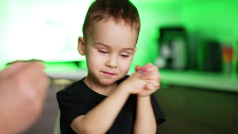Cheerful Caucasian toddler chewing food and waving hands. Mom is holding a spoon waiting for kid to take.