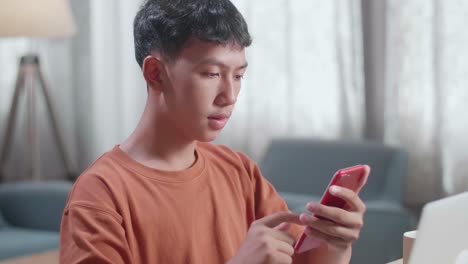 아시아 소년 신발 디자이너가 집에서 노트북으로 작업하는 동안 스마트폰을 보고 있습니다.