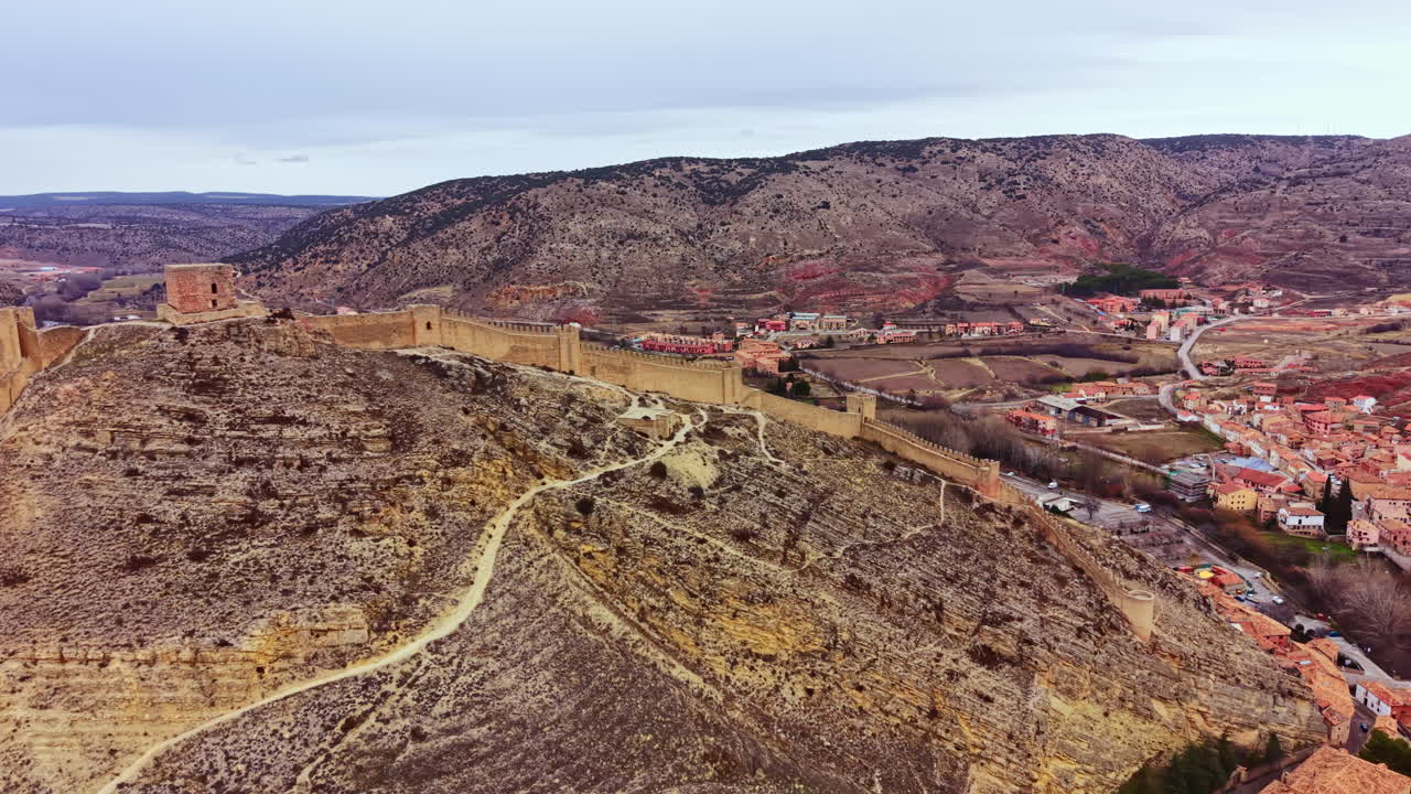 Castelli si ergono sulla collina vicino a un paese con strade che si snodano attraverso un terreno roccioso in Spagna, in una giornata nuvolosa.
