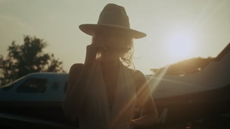 woman in a hat and dress near a private jet at sunset