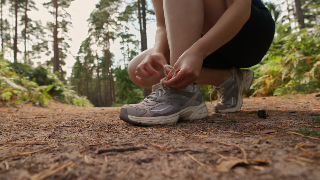 primer plano de una mujer atando los cordones de su zapato de entrenamiento antes de hacer ejercicio corriendo por la pista a través del bosque disparado en tiempo real 2