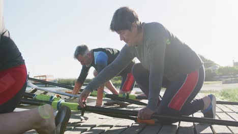 Senior-caucasian-woman-and-teammates-preparing-rowing-boat-in-a-river