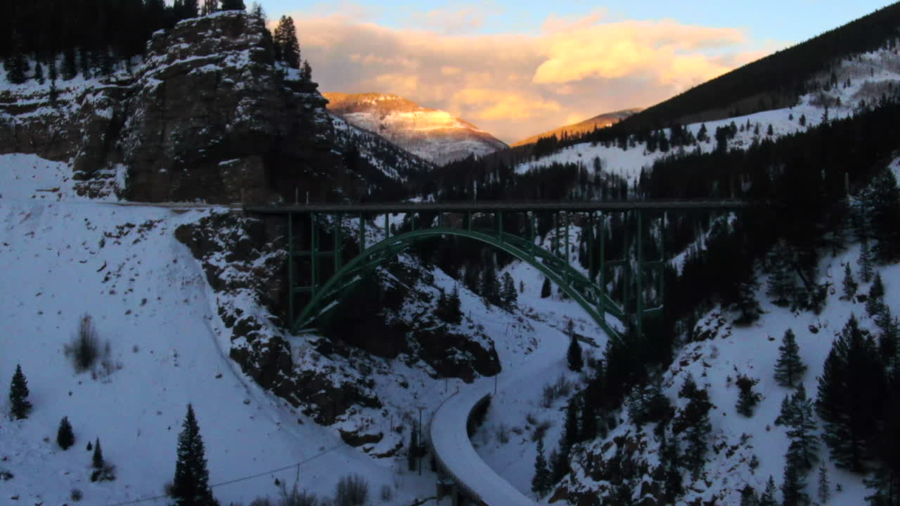 avión no tripulado cinematográfico vail avon acantilado rojo icónico colorado bajo el puente mitad del invierno coches conduciendo en la nieve tarde anaranjado puesta de sol paisaje de montaña movimiento hacia adelante