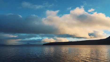 a beautiful driving shot of arctic peaceful sea and mountain slope under a cloudy blue sky, iceland, westfjords