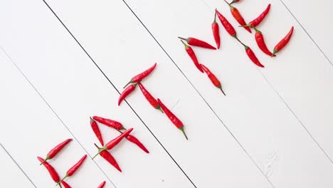 A-words-EAT-ME-formed-with-small-red-chilli-peppers--Placed-on-white-wooden-table