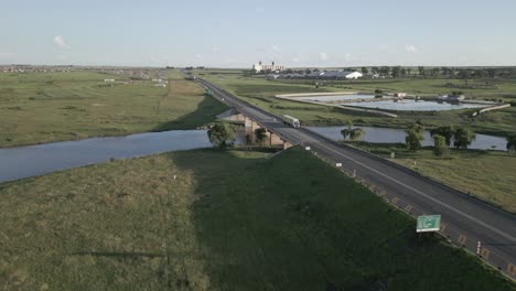 Rückzüge-Aus-Der-Luft-Von-Der-Brücke-über-Den-Schmalen-Fluss,-Kleine-Stadt-In-Der-Ferne