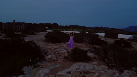 woman meditating in yoga position on a cliff overlooking the sea at sunset in ibiza. unique aerial view flight fly reverse drone