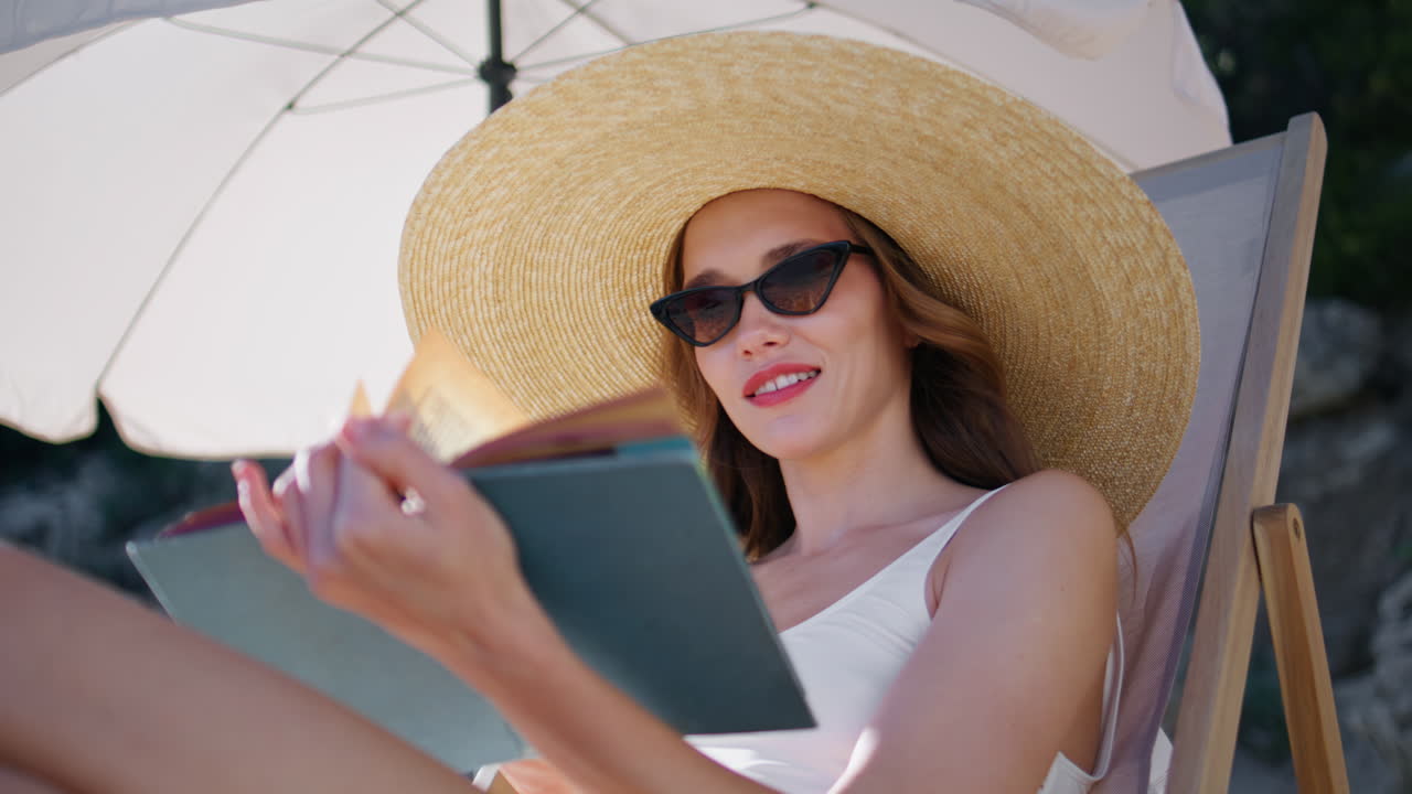 Woman reading book beach wearing straw hat closeup. Smiling lady enjoying novel