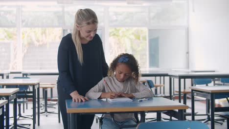 friendly female school teacher helping mixed girl with homework