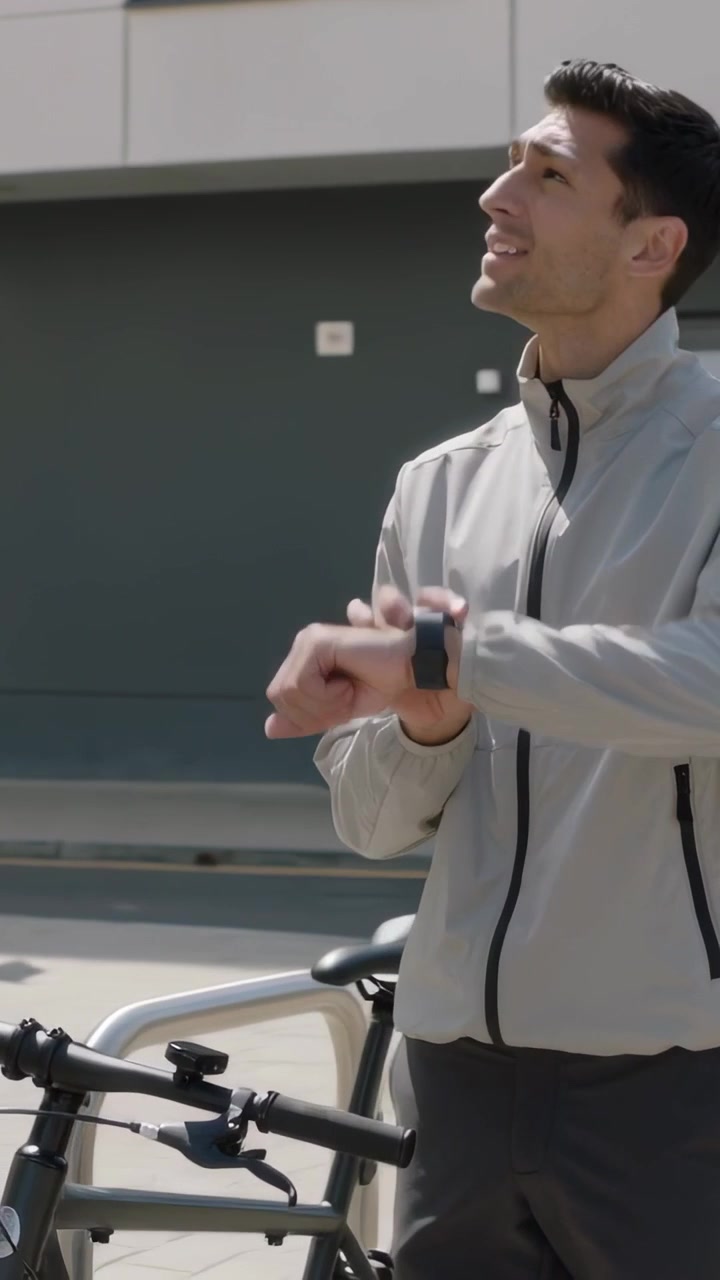 Vertical video: Tapping smartwatch, man preparing bike for ride at doorway, wearing gray jacket
