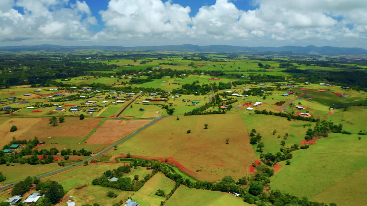 vista aérea de campos verdes, cielo azul nublado y ciudad en la región de las mesetas de atherton, queensland, australia - disparo de drones