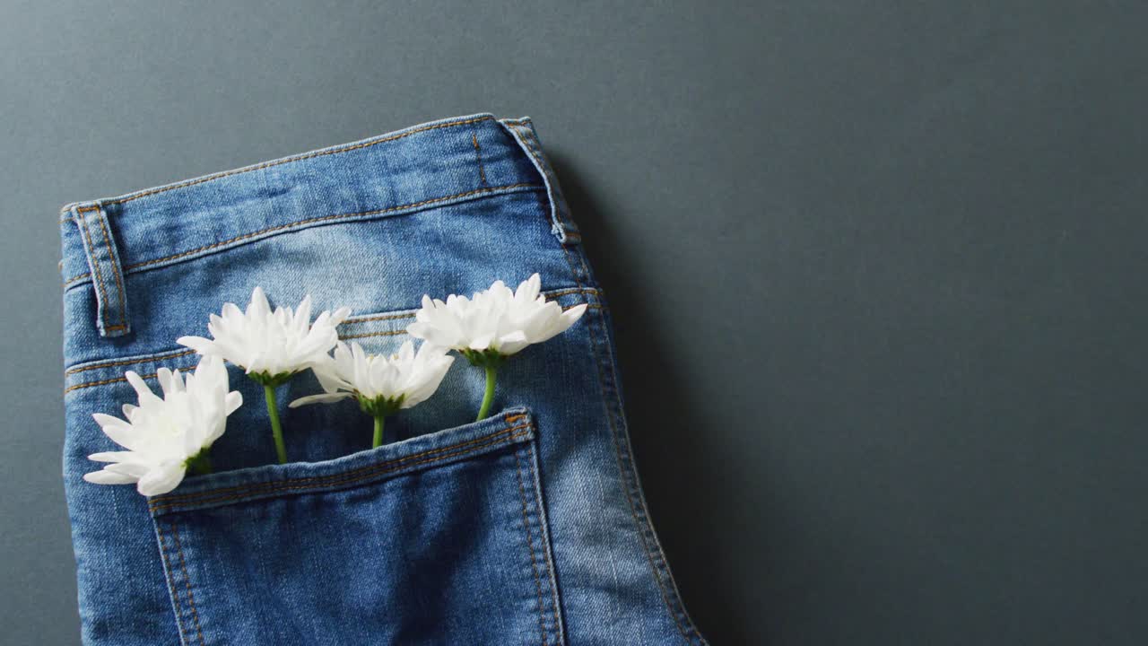 Primo piano di jeans con fiori bianchi su sfondo grigio con spazio per il testo