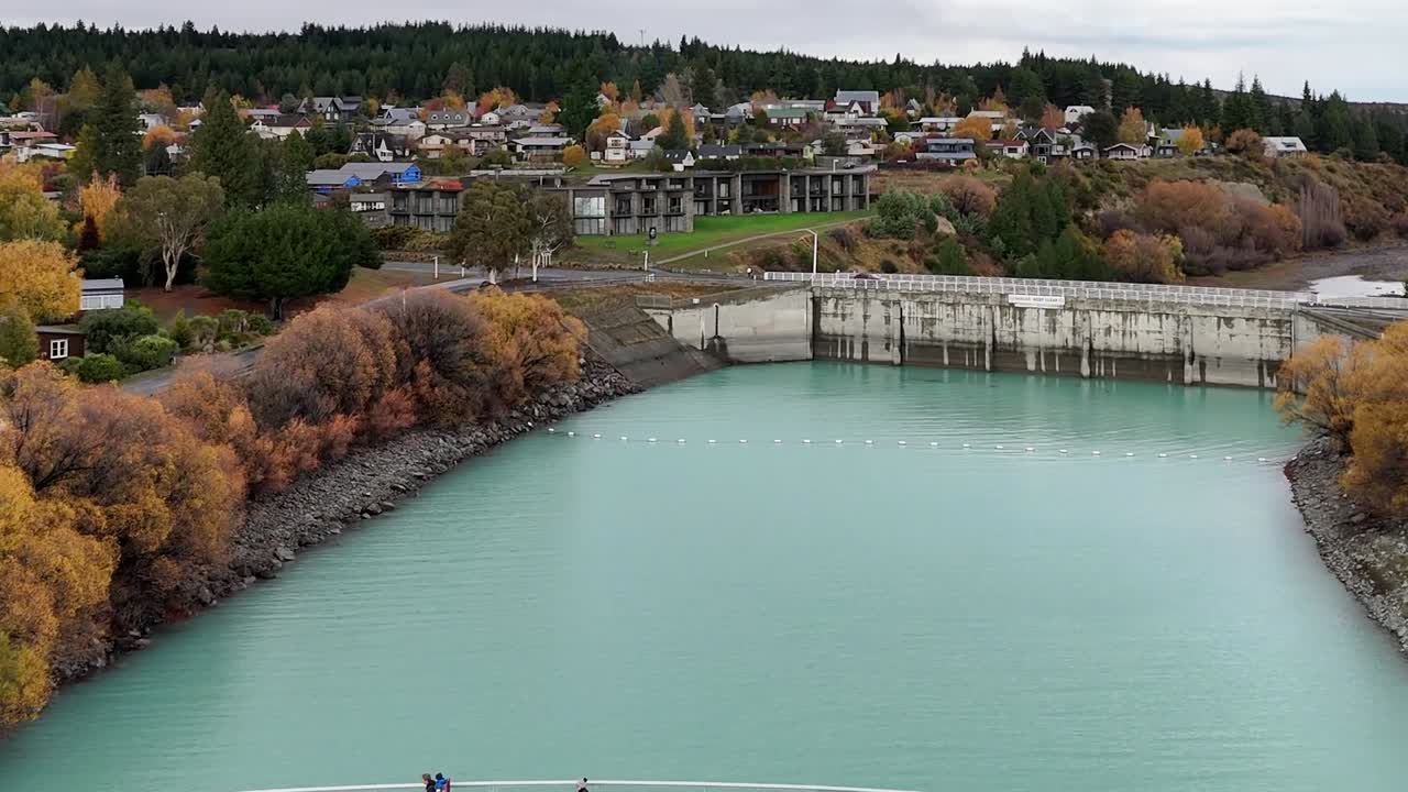 Riprese aeree riprendono un ponte pedonale bianco che attraversa acque turchesi circondato da alberi autunnali colorati