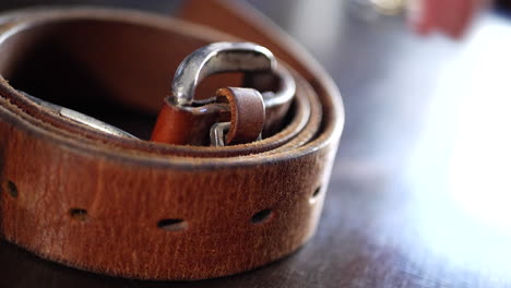 A-man-placing-his-worn-out-vintage-leather-belt-and-buckle-on-a-table-after-a-hard-days-work-in-slow-motion