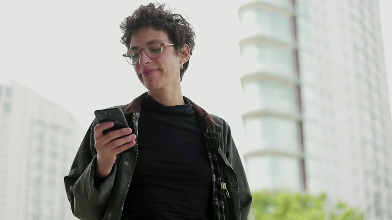 mujer sonriente con gafas usando un teléfono inteligente al aire libre