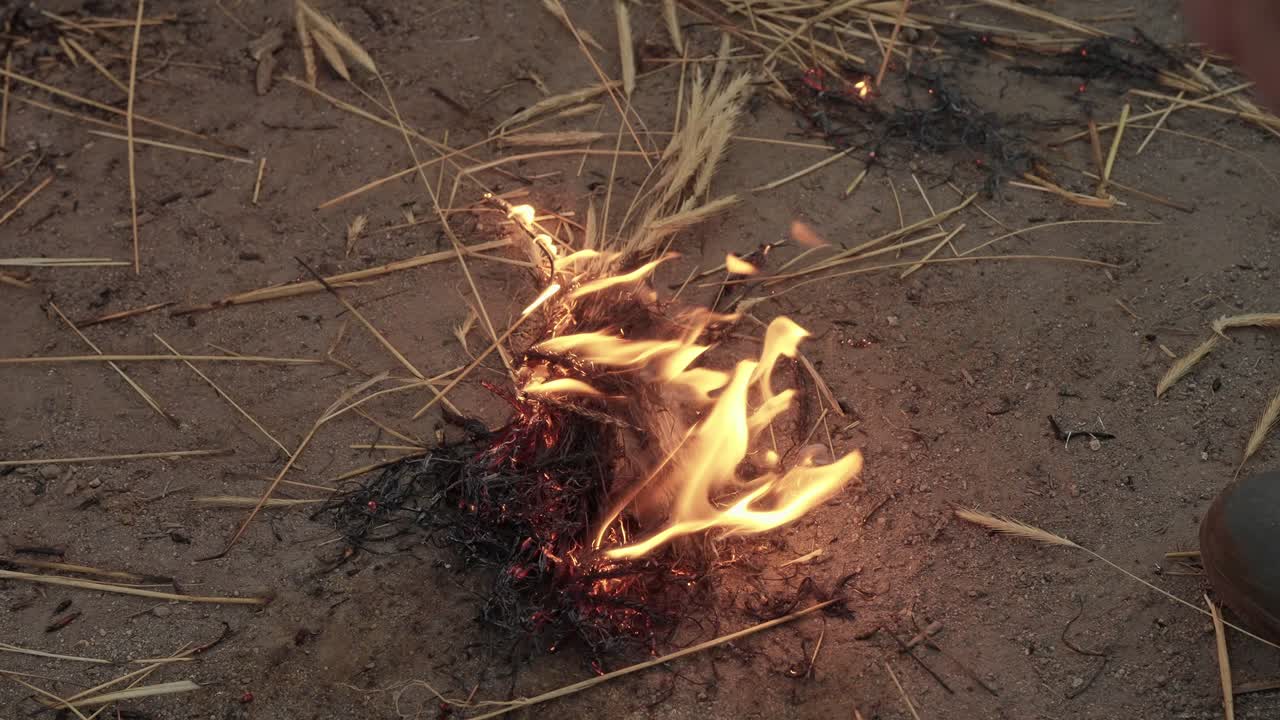 straw pressed to flames ignites small bundle on bare dirt for cleaning process